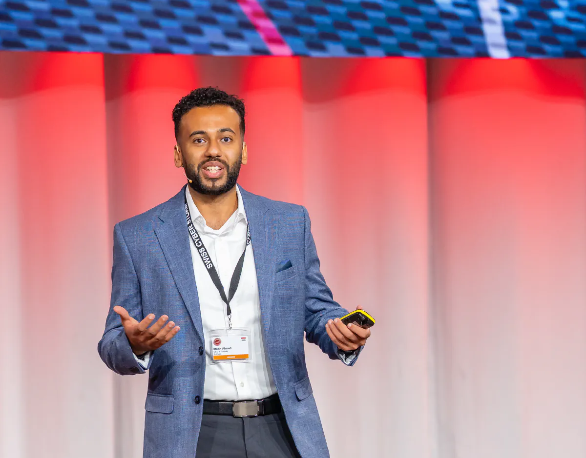 Speaker in a blue blazer presenting with a headset microphone and presentation remote at Swiss Cyber Storm.